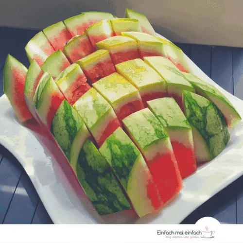 Watermelon cut in sticks on white square plate and dark wooden ground.