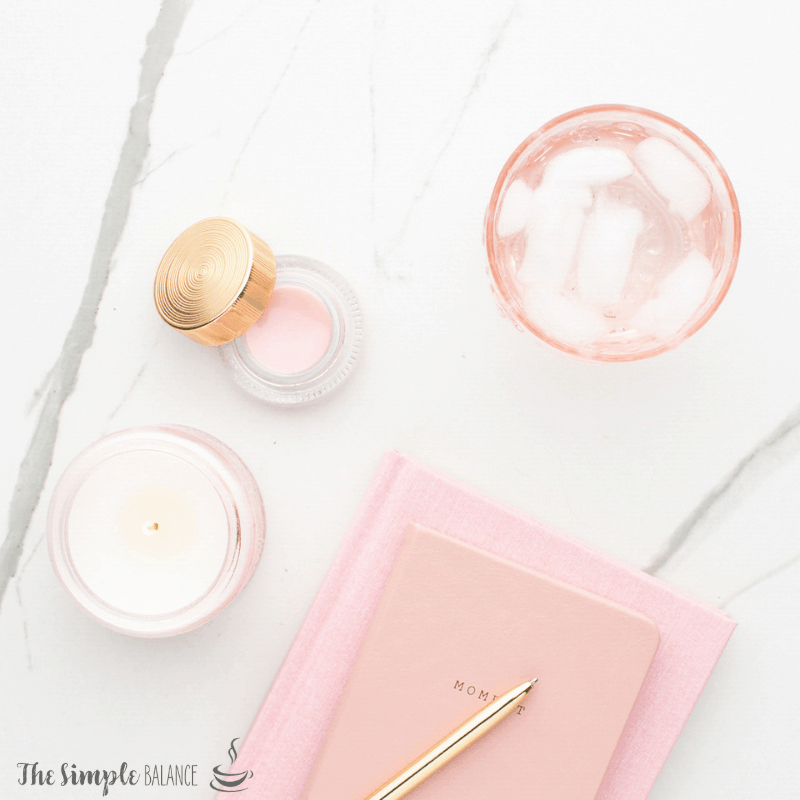 Calming self-care setup with pink candle, MOM notebook, golden pen, and refreshing drink on marble.