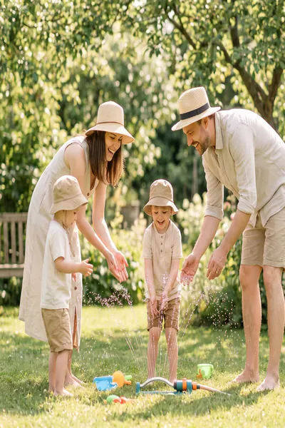 Family with kids relaxing in a shady garden, using water and sun hats to stay cool from the heat